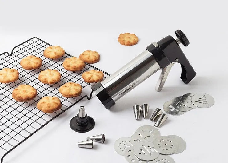 Stainless steel biscuit press machine with assortment of cookie moulds and piping nozzles on a kitchen worktop