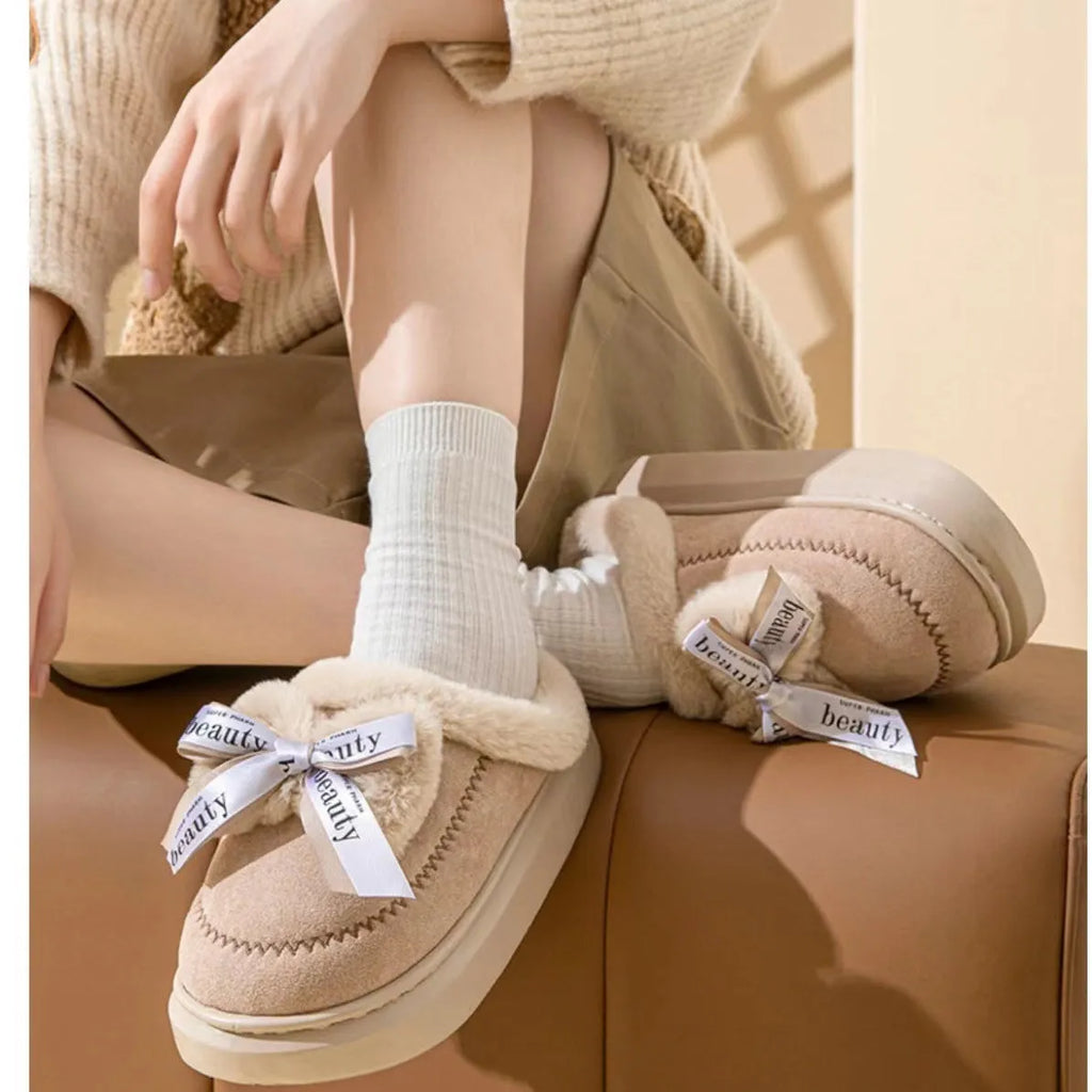 Beige women's suede half slippers with a black ribbon bow and thick cotton sole.