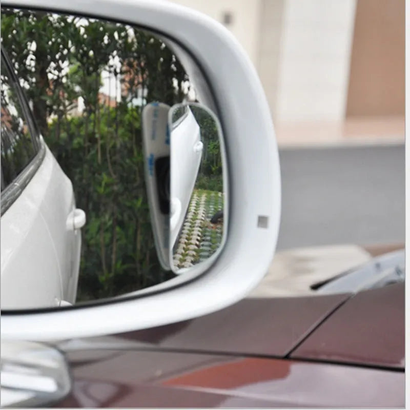 Glass adjustable blind spot mirror with angle bracket shown next to a vehicle rearview mirror.