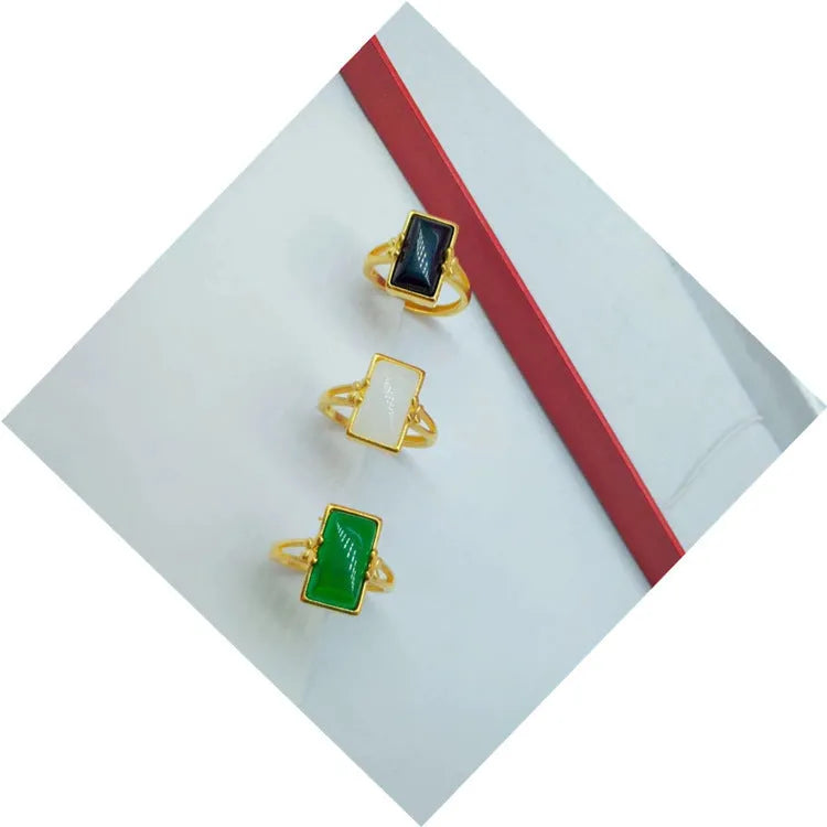 Adjustable gold-plated brass ring with a black artificial gemstone on a neutral background.