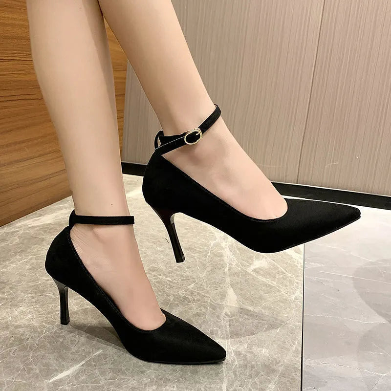 Women's black stiletto heel pumps with skull pattern and buckle detail on wooden floor