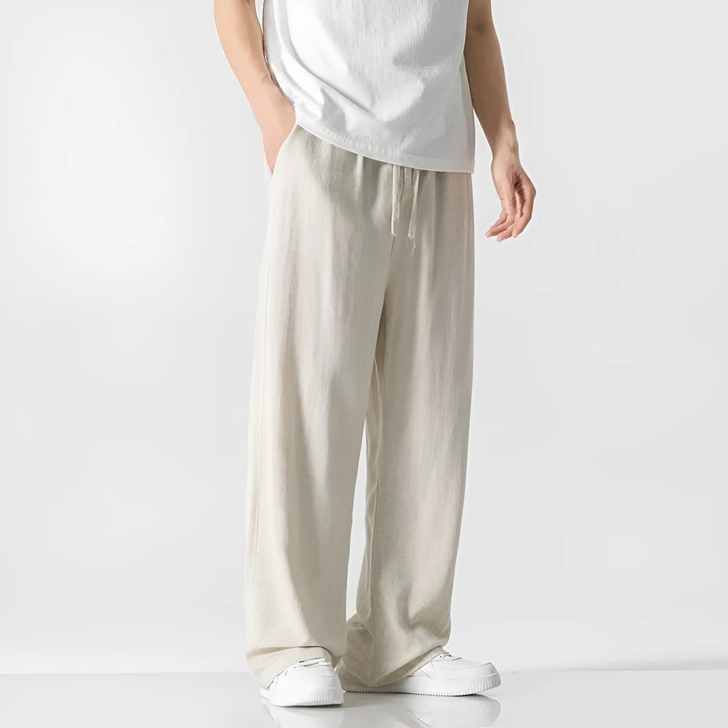 Men's beige loose straight-leg linen trousers with a drawstring waist, shown in a casual summer setting.