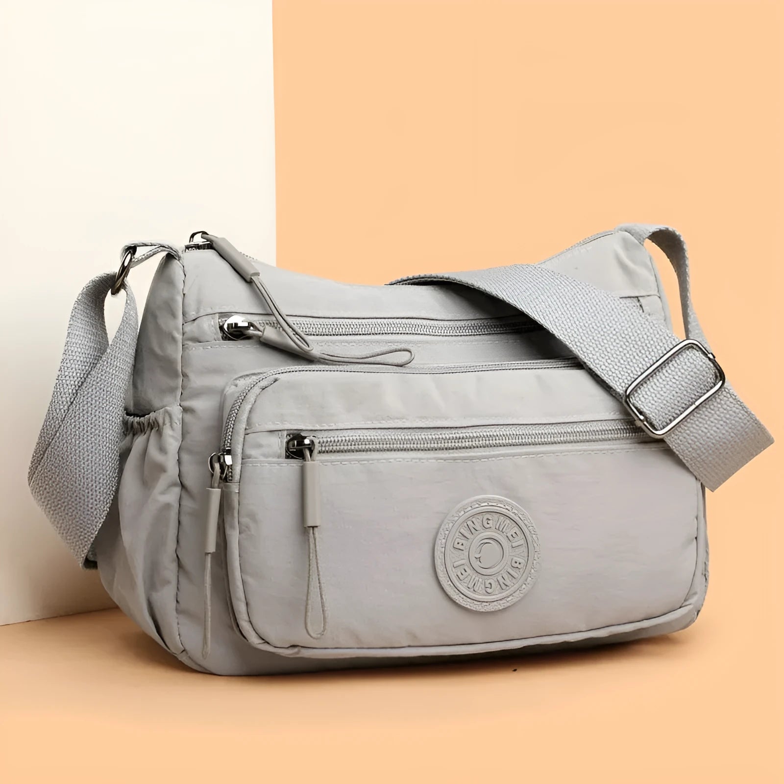 Grey water-repellent nylon crossbody bag showing front three-dimensional pocket and adjustable shoulder strap.