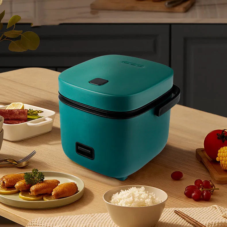 Green 1.2L mini rice cooker with metal body, button controls, and steaming plate on a worktop.