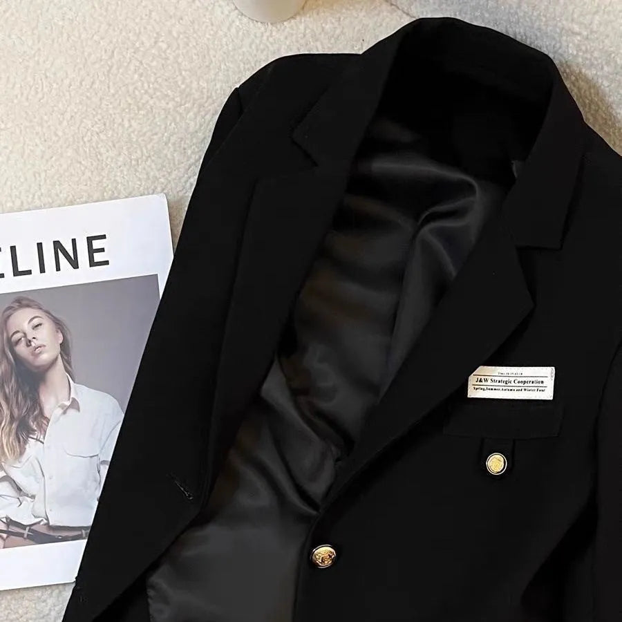Black loose-fit women's short suit coat with long sleeves and pockets on a hanger.