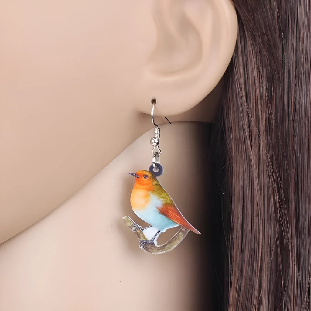 Close-up of blue titmouse and geometric zodiac pendant earrings made from printed acrylic.