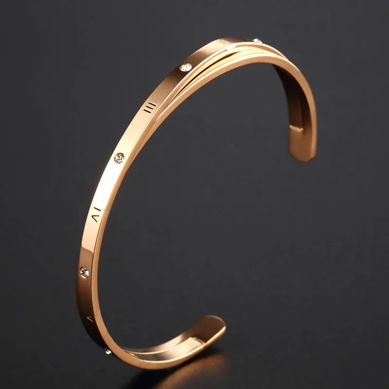 Open-ended stainless steel bracelet with inlaid zircon stones and a love charm in rose gold colour.