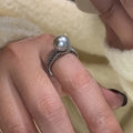 Women's adjustable copper ring with black pearl and geometric open design on an index finger.