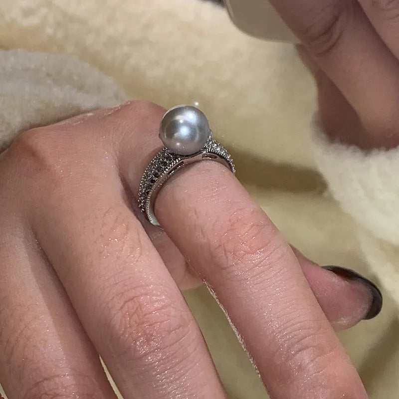 Women's adjustable copper ring with black pearl and geometric open design on an index finger.