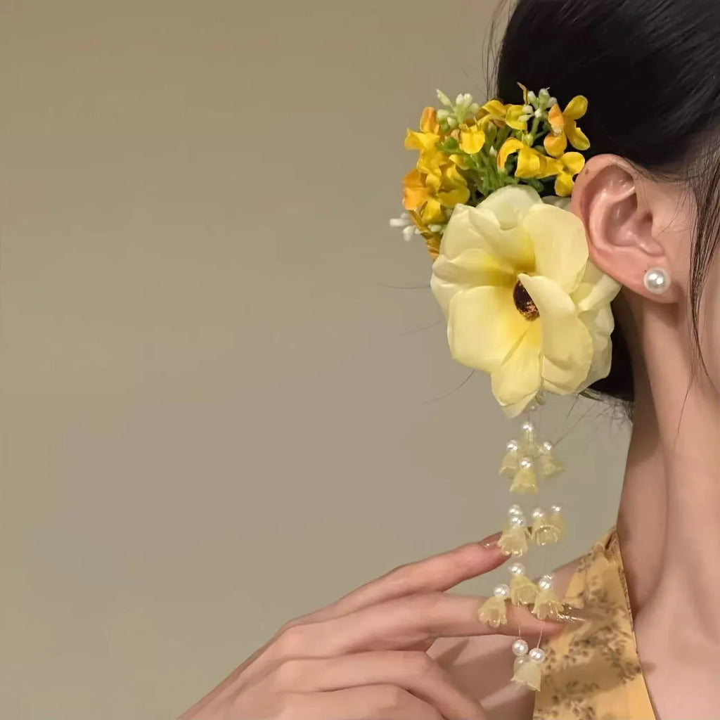 Yellow flower tassel side clip hair accessory for women on a purple background.