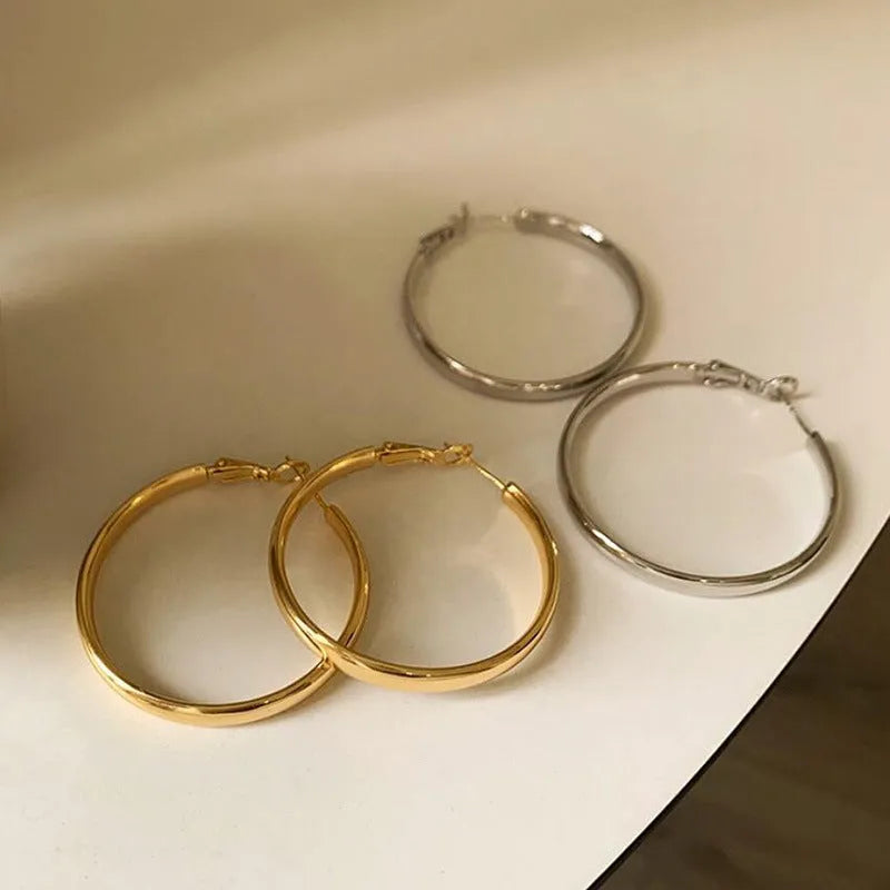 A pair of large, circular gold metal earrings against a plain background.