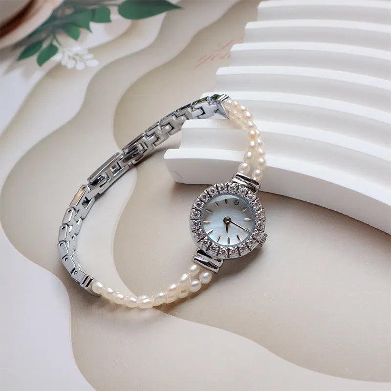 Light gold women's bracelet watch with freshwater pearls, an 18mm round dial, and a stainless steel folding buckle.