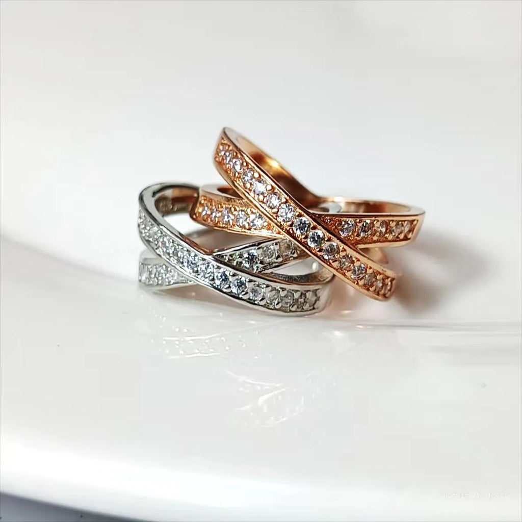 Silver or rose gold metal cross ring with micro-inlaid zircon accents on a plain background.