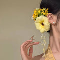 Yellow flower tassel side clip hair accessory for women on a purple background.
