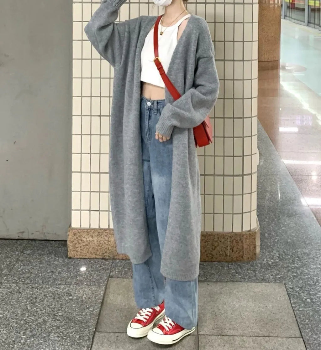 Loose large dark grey knitted cardigan with a 3D pattern, worn open over a top.