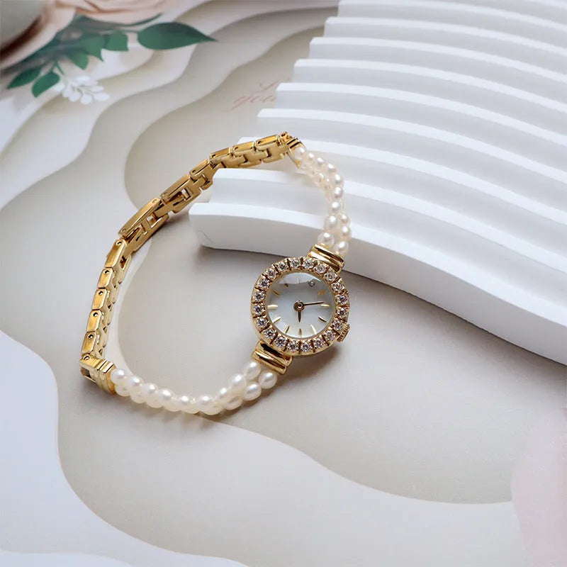 Light gold women's bracelet watch with freshwater pearls, an 18mm round dial, and a stainless steel folding buckle.