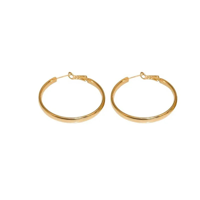 A pair of large, circular gold metal earrings against a plain background.