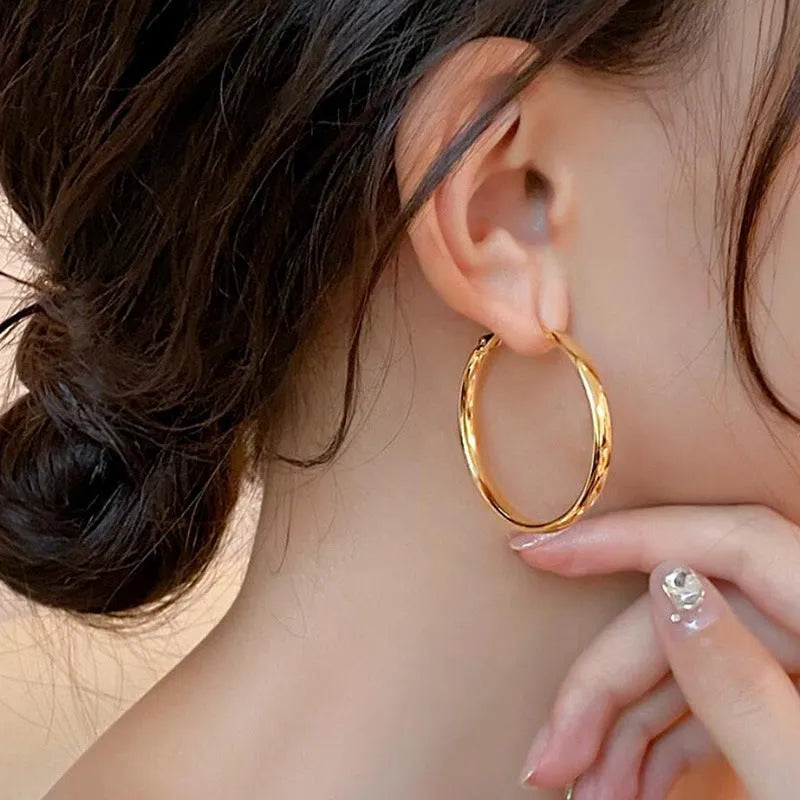 A pair of large, circular gold metal earrings against a plain background.