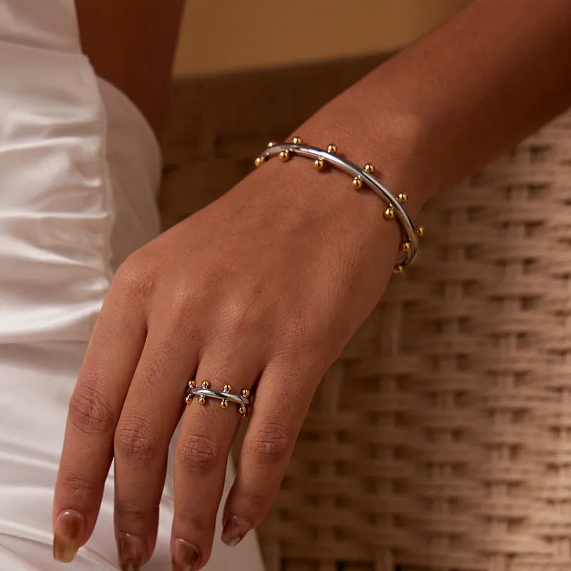 Stainless steel C-shaped bean beads with textured rivet design in gold, steel, and steel gold colours next to an alloy bracelet.