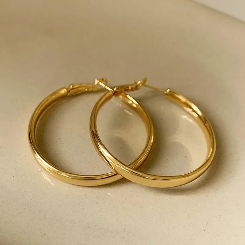 A pair of large, circular gold metal earrings against a plain background.