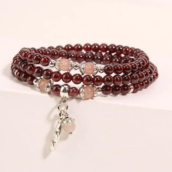 Wine red garnet crystal bracelet with flower-shaped charm on a model's wrist.