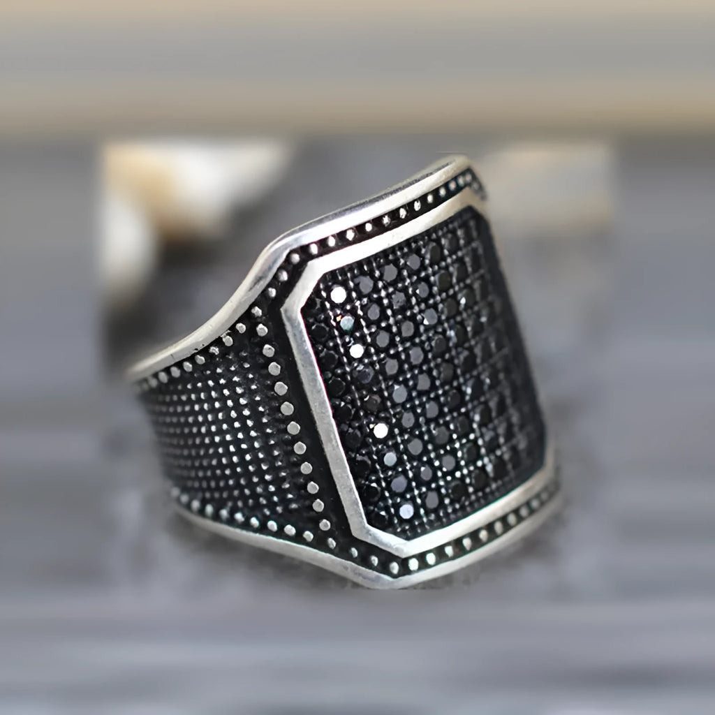 A black alloy ring with copper inlay and a centred zircon stone, shown on a finger.