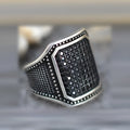 A black alloy ring with copper inlay and a centred zircon stone, shown on a finger.