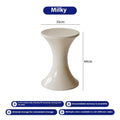 A white hourglass-shaped plastic shoe changing stool on a wooden floor.