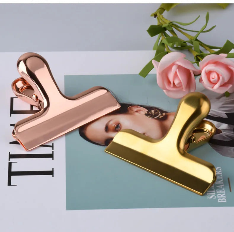 Gold stainless steel dovetail clip holding a stack of papers on a desk
