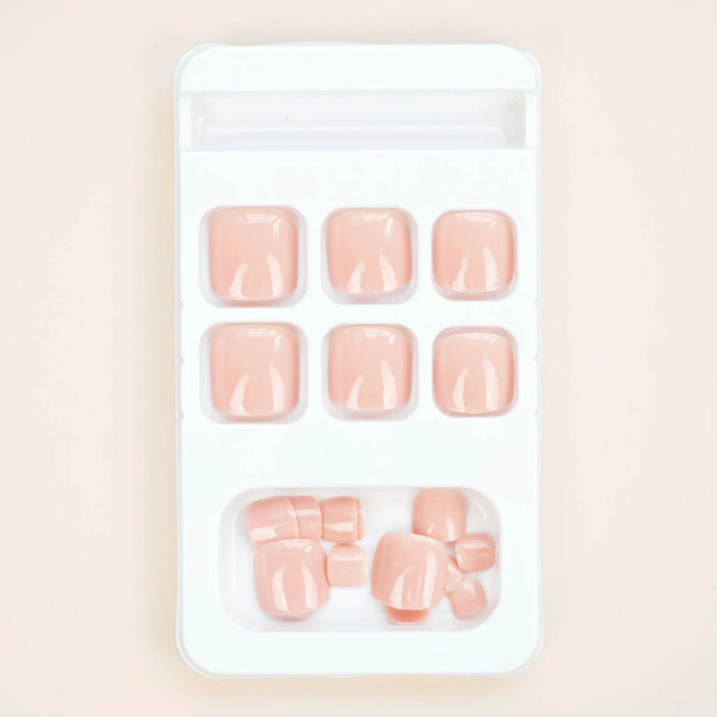 Finished plastic toe nail stickers in J-52 skin colour with glue tube on white background.