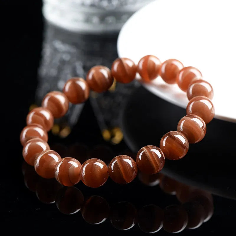 Natural old mine rhodochrosite round bead bracelet with geometric and Ruyi design on a wrist.