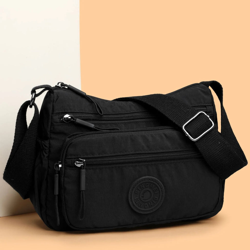 Grey water-repellent nylon crossbody bag showing front three-dimensional pocket and adjustable shoulder strap.