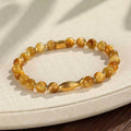 Close-up of a women's bracelet with small fish-shaped Tiger Eye stone beads in yellow, red, or gold colours.