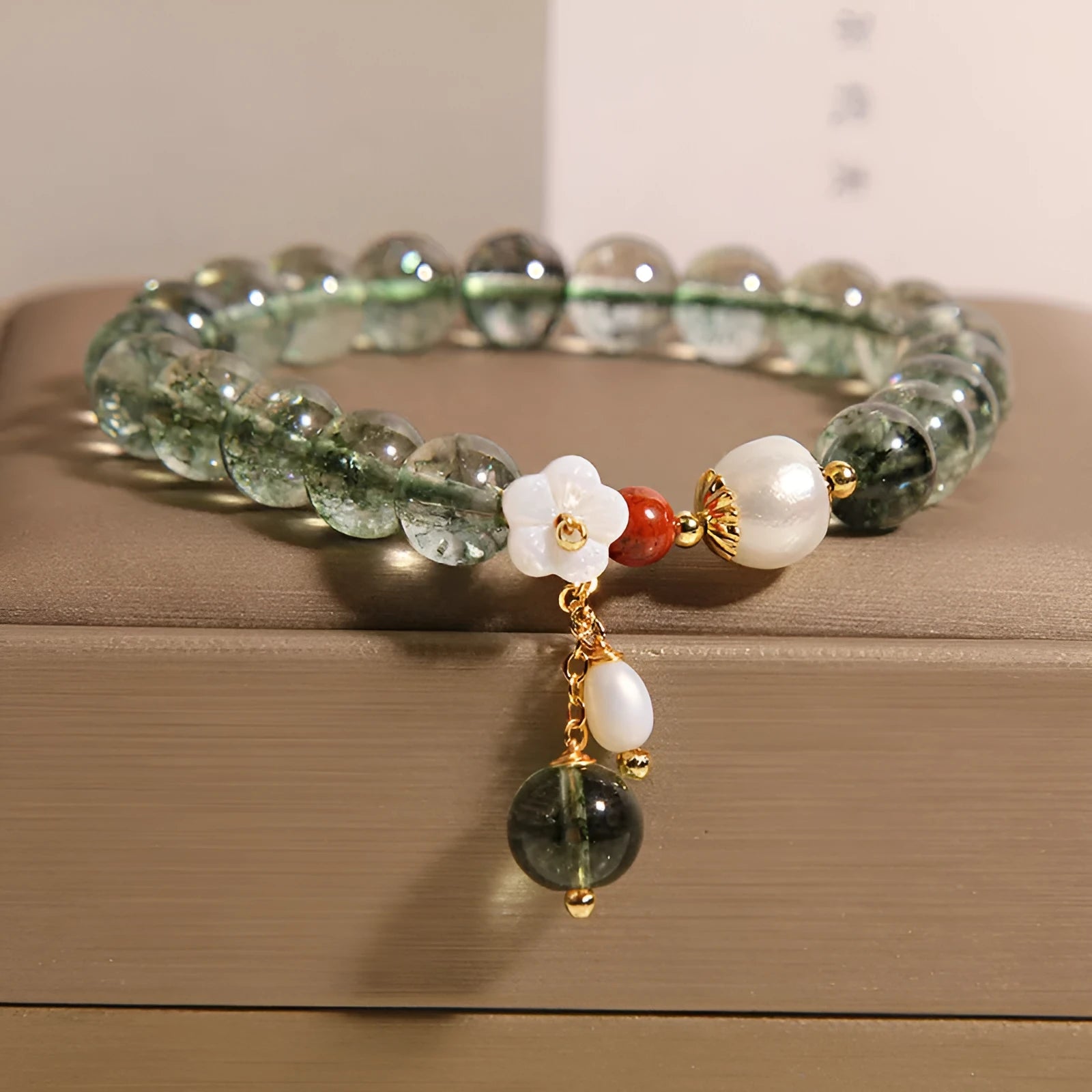 Green phantom quartz crystal bracelet with shell flower charm on a woman's wrist