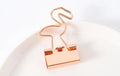 Gold metal clip with a decorative bow charm, shown holding papers.