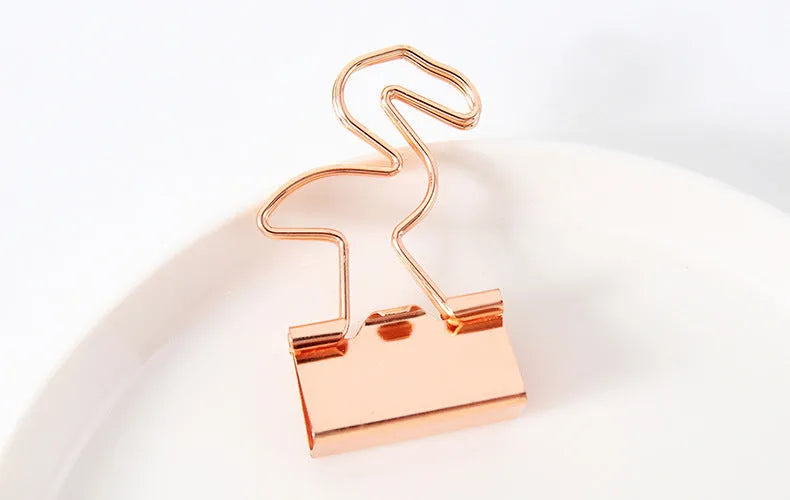 Gold metal clip with a decorative bow charm, shown holding papers.