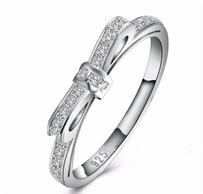 Silver coloured bow-shaped ring with sparkling rhinestone zircon crystals on a finger.