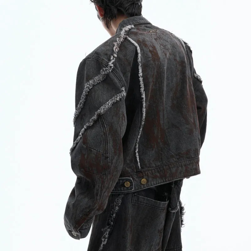 Black distressed raw-edge denim coat with padded shoulders and splash-dye gradient, paired with matching black pants.