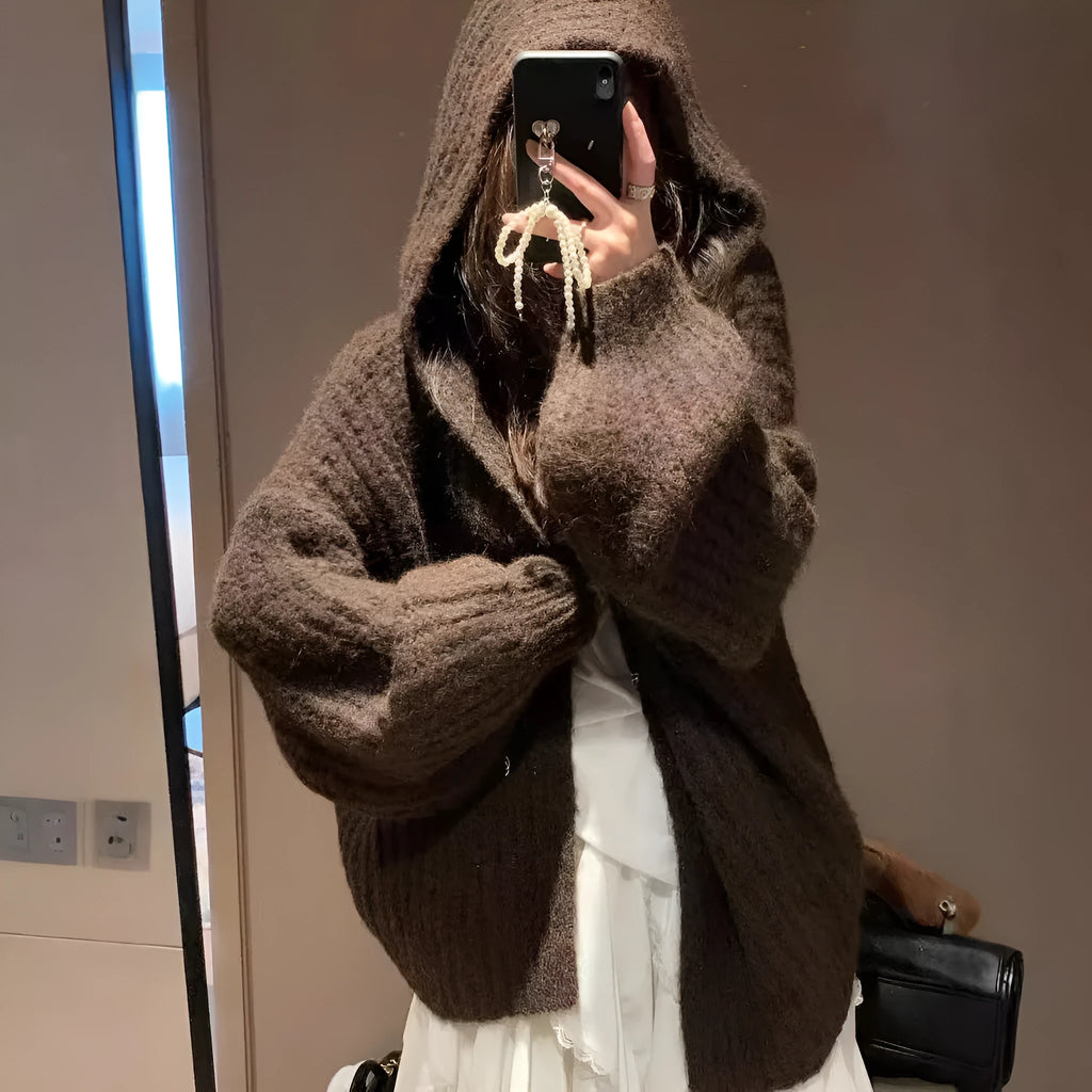 A woman wearing a thick, loose-fit, dark grey hooded sweater cardigan with a retro design.