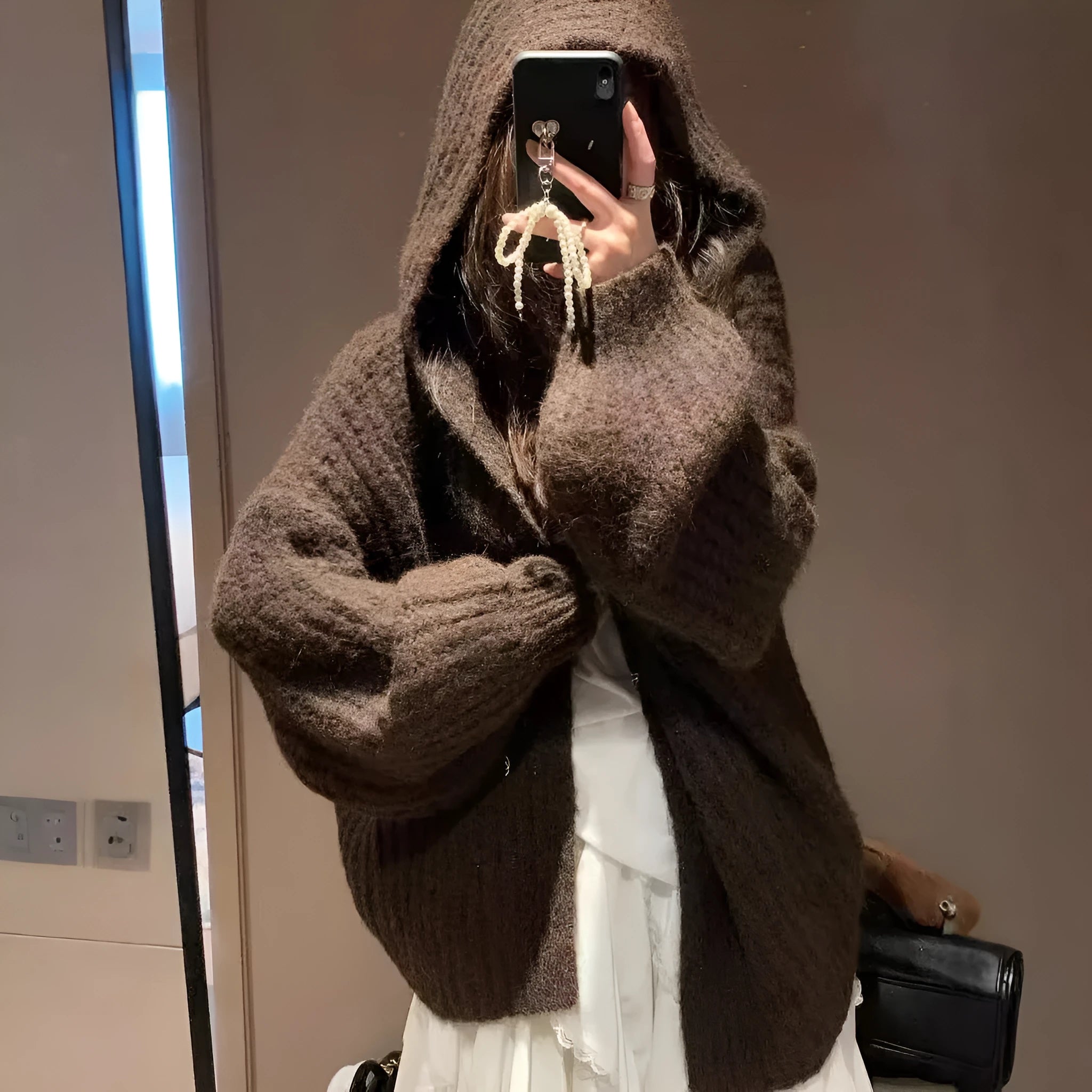 A woman wearing a thick, loose-fit, dark grey hooded sweater cardigan with a retro design.