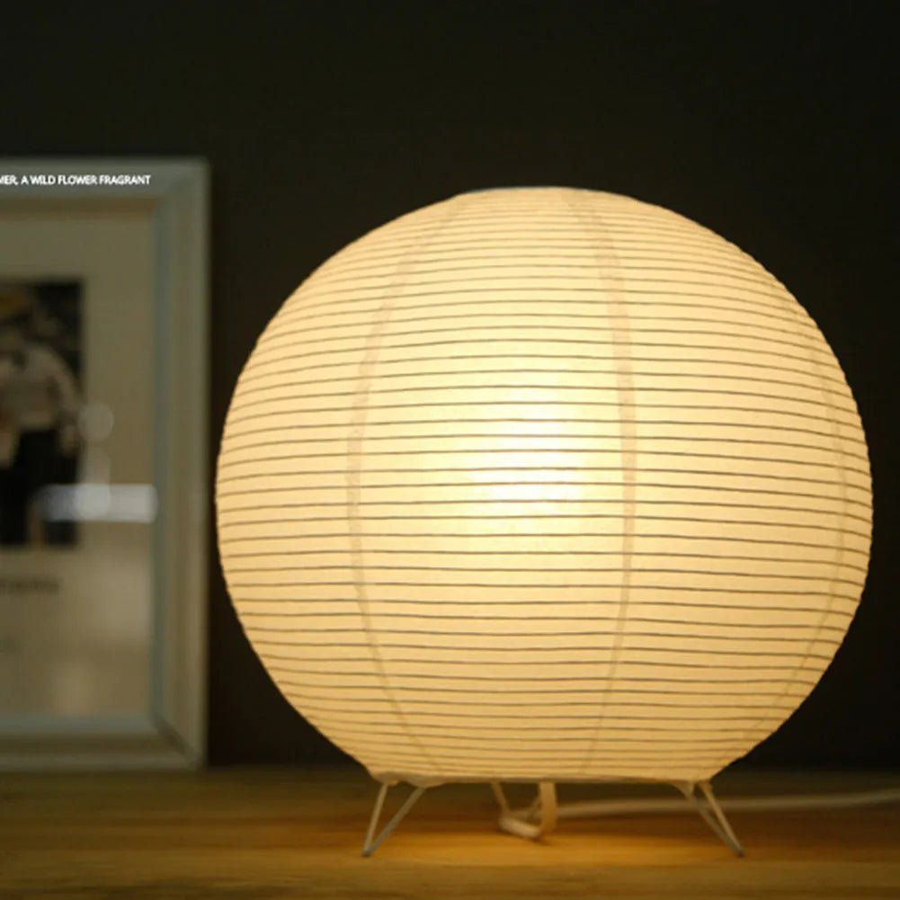 White handcrafted rice paper table lamp with either a circular or rectangular shade on a wooden desk.