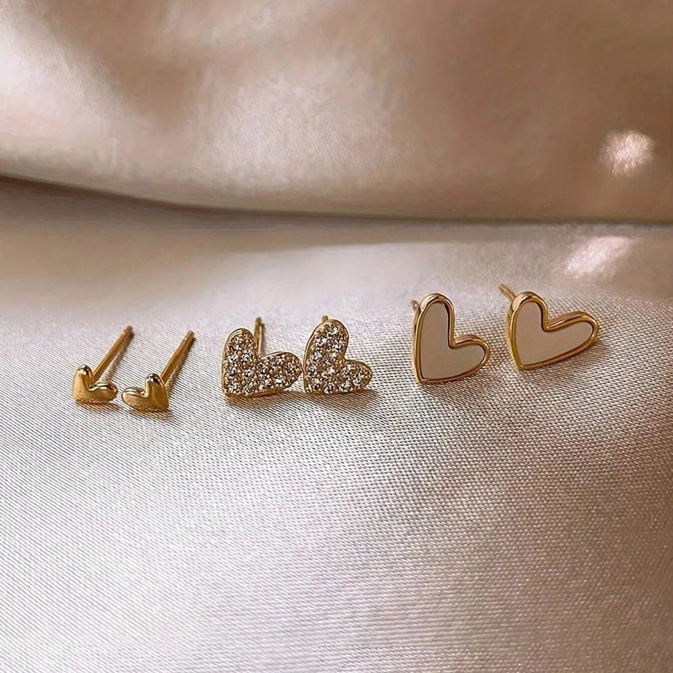Three pairs of women's heart-shaped alloy earrings in gold, black, black and white, and pink colours