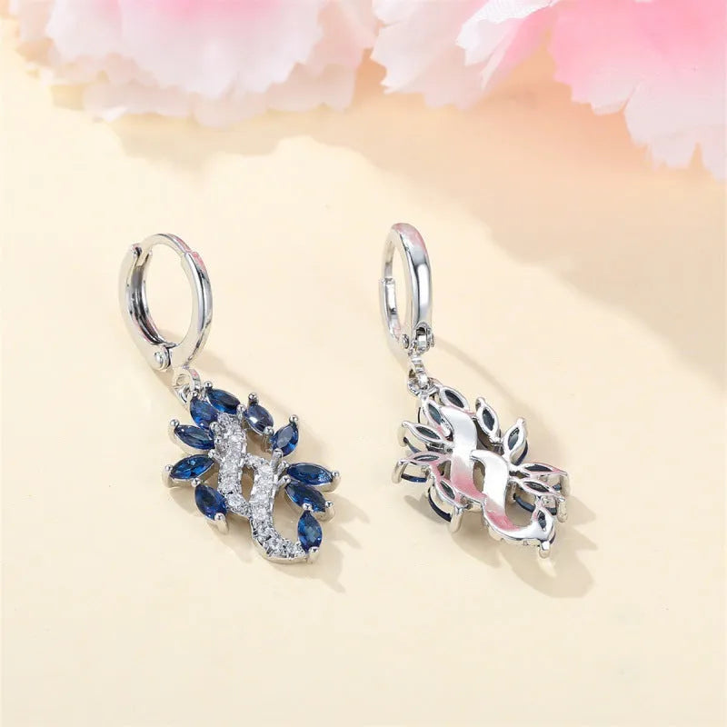 A pair of platinum sapphire blue alloy drop dangle earrings for women on a plain background.