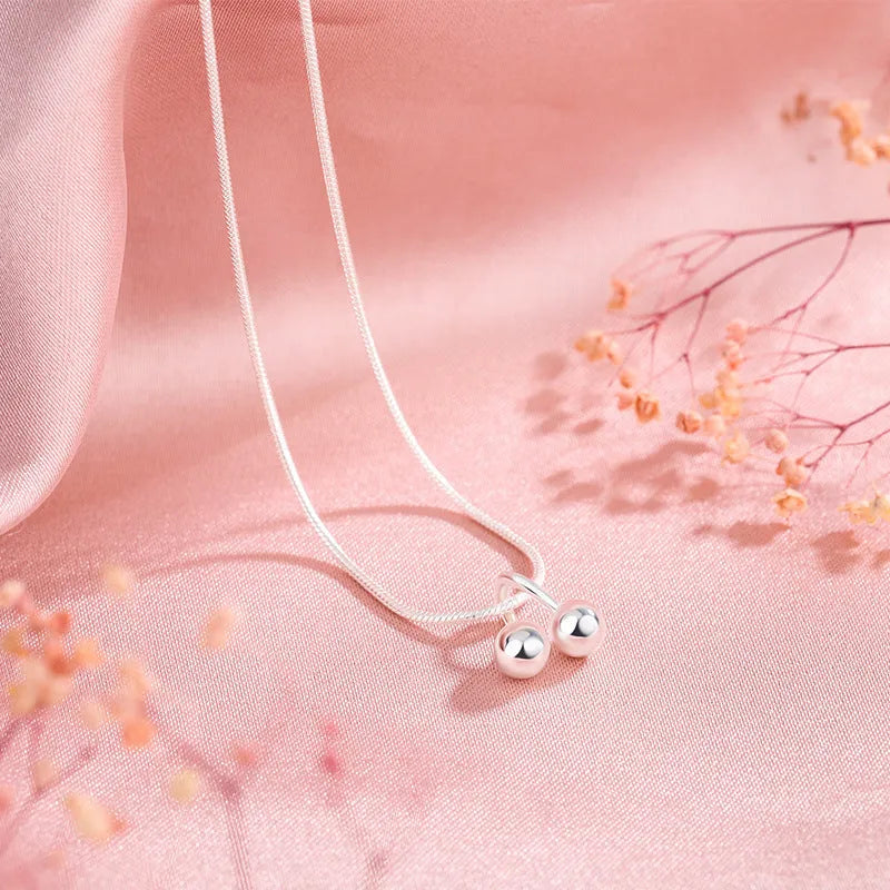 Silver cherry necklace for women with adjustable snake bone chain on a grey background.