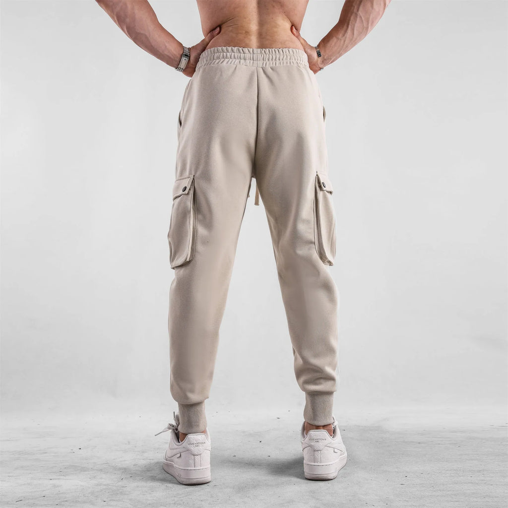 Men's loose light grey cotton trousers with ankle ties and multiple pockets laid flat.