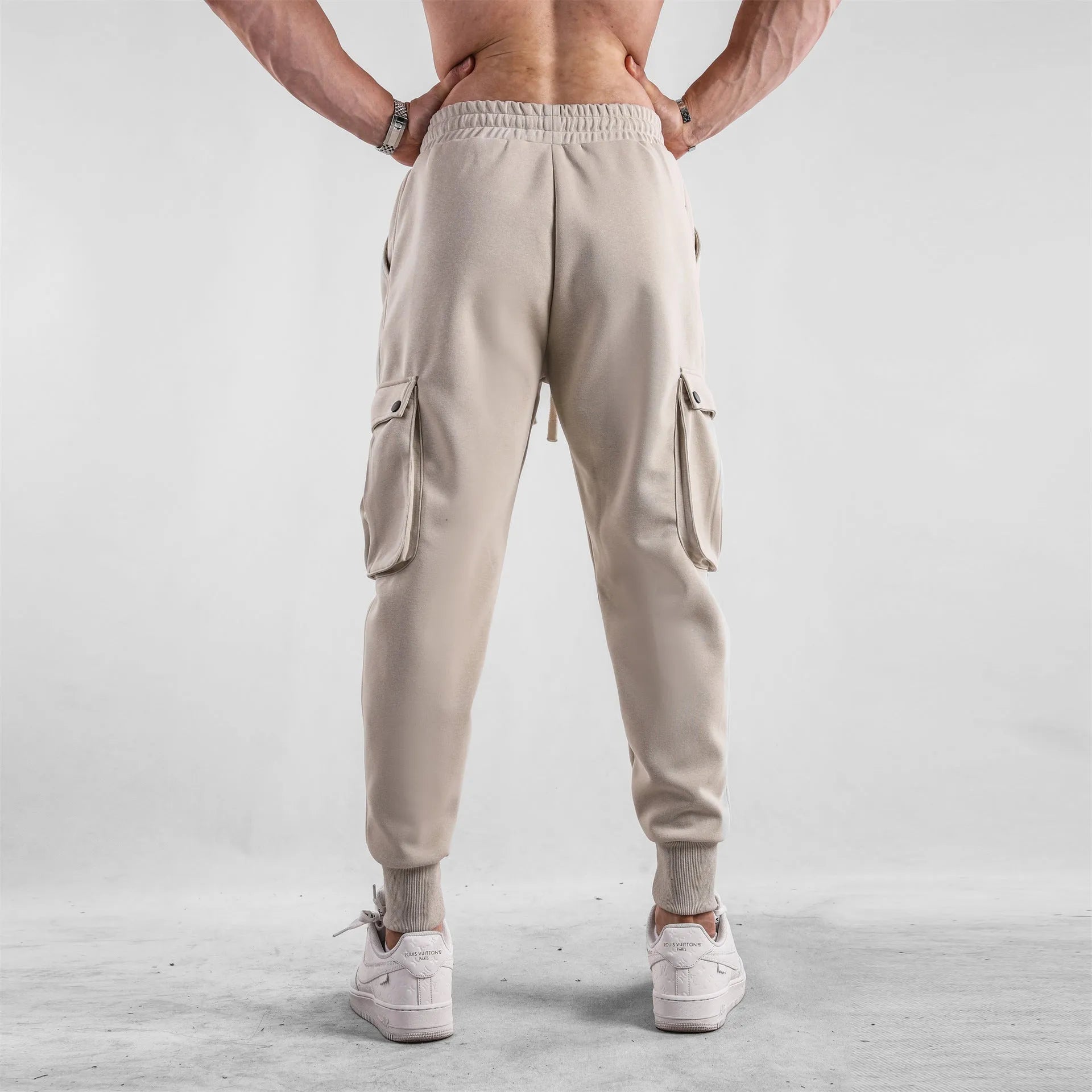 Men's loose light grey cotton trousers with ankle ties and multiple pockets laid flat.