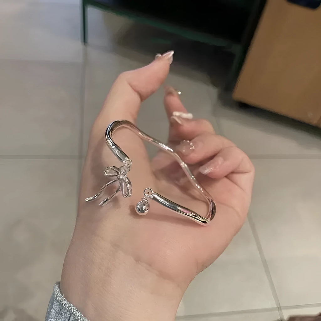 Silver adjustable girlfriends bracelet with bow and bell charm on a wrist.