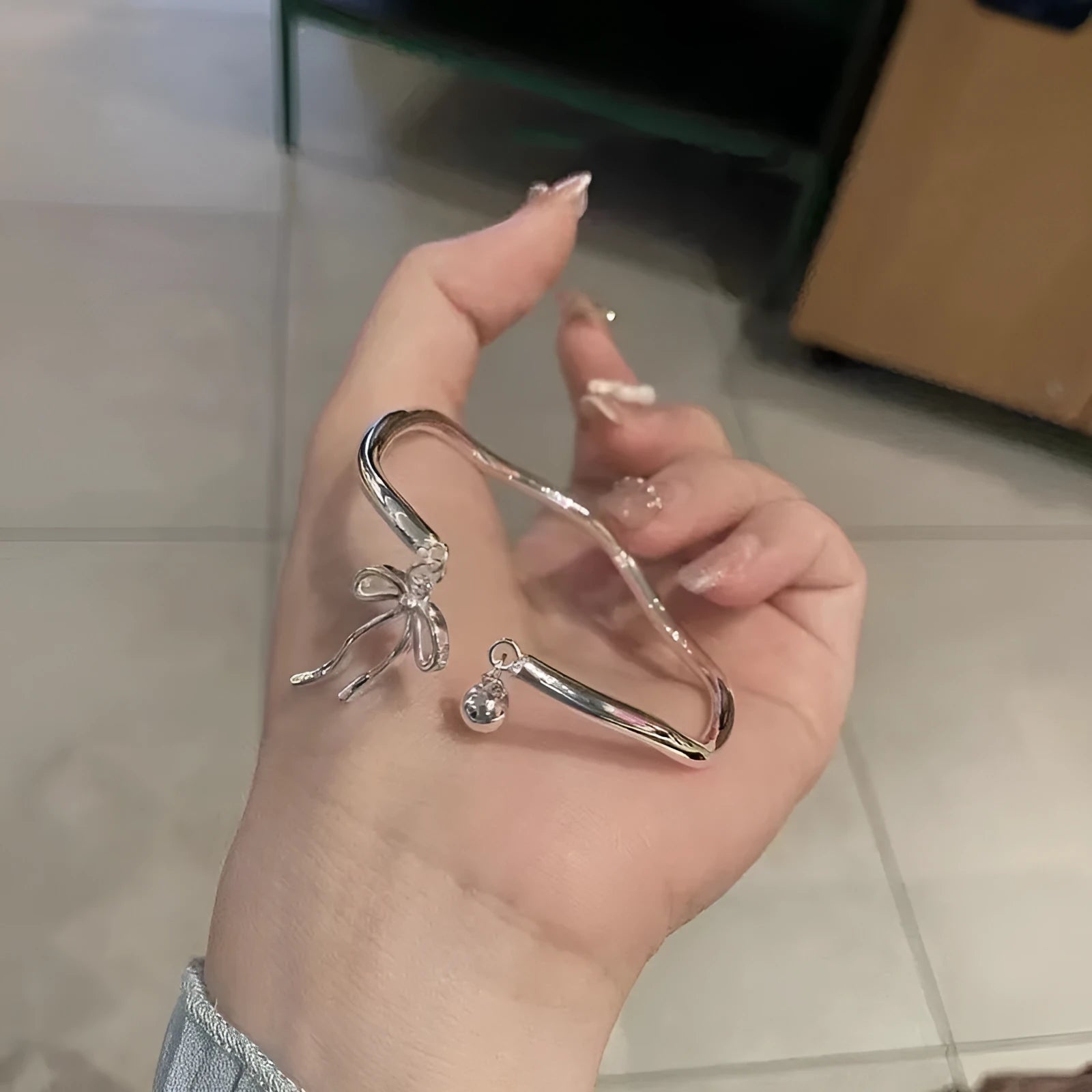 Silver adjustable girlfriends bracelet with bow and bell charm on a wrist.