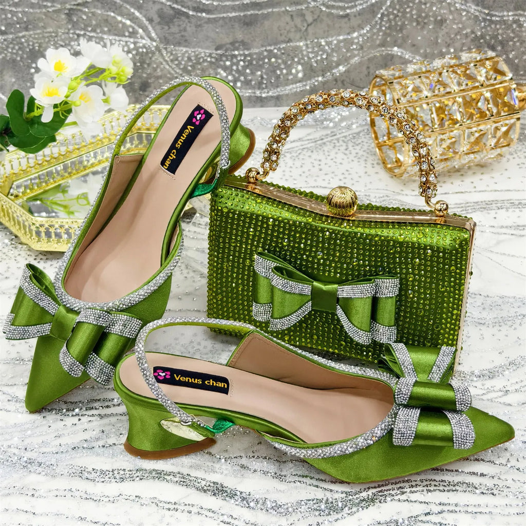 Women's black pointed sandals with a square rhinestone buckle and mid heel, next to a matching clutch bag.