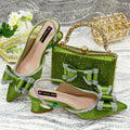 Women's black pointed sandals with a square rhinestone buckle and mid heel, next to a matching clutch bag.